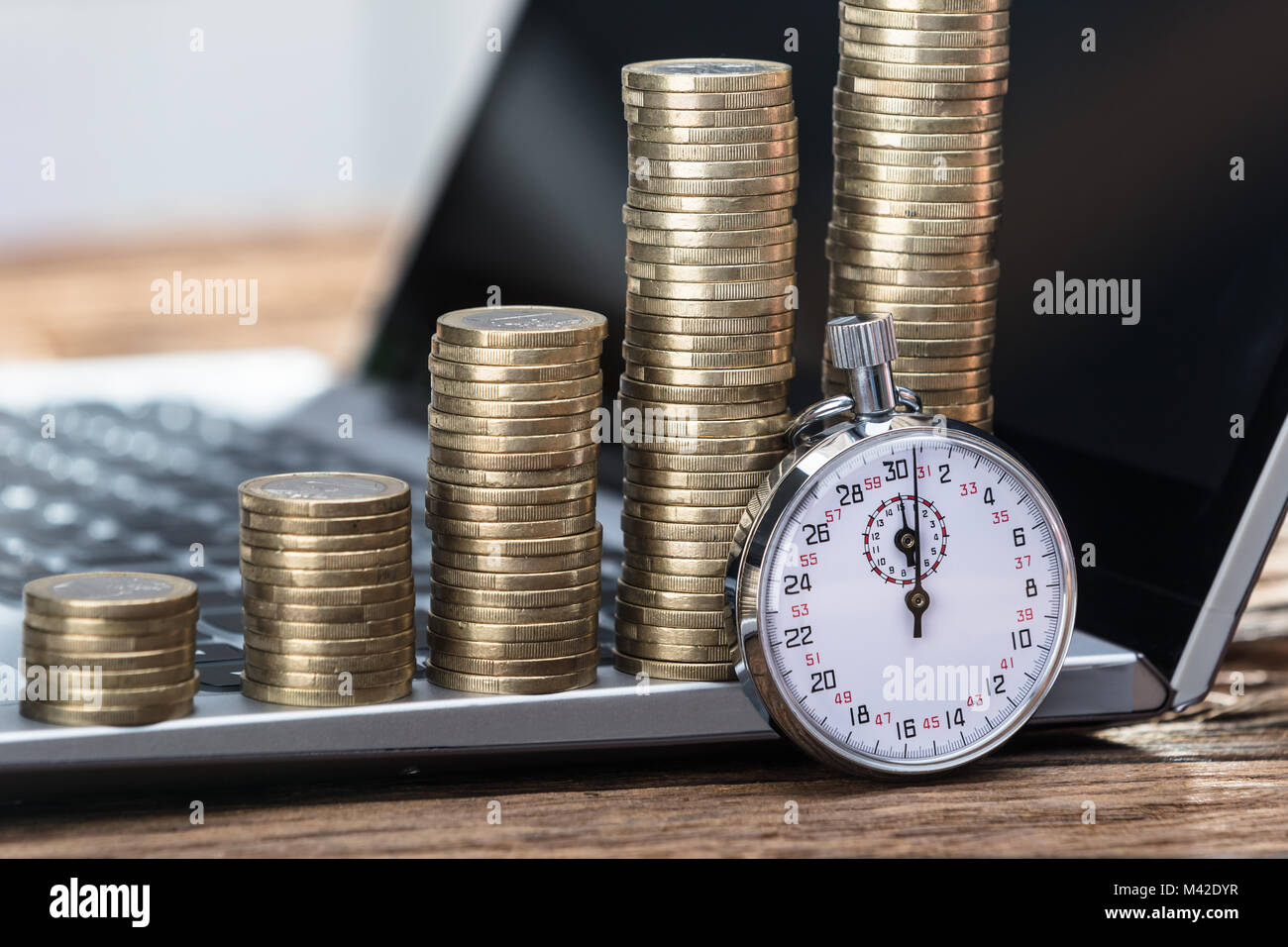 Closeup Of Stopwatch With Increasing Stacked Coins On Laptop Stock