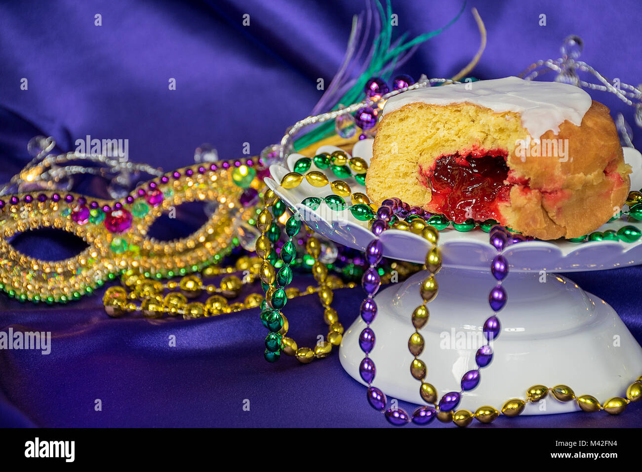 close up of jelly filled paczki with Mardi Gras beads and mask on purple satin Stock Photo