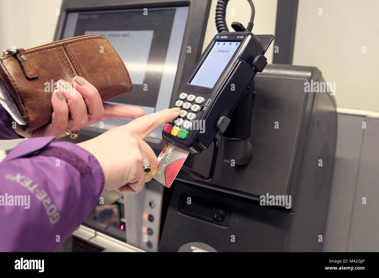A female shopper using a chip and pin card reader machine to pay for goods using a credit card. She is entering her pin number on the rubber keypad Stock Photo