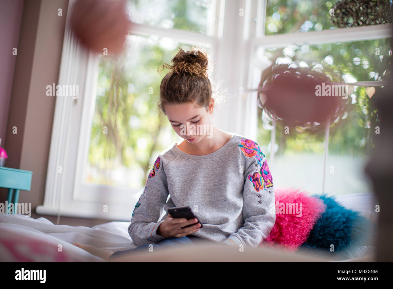 Teenager in bedroom looking at smartphone Stock Photo