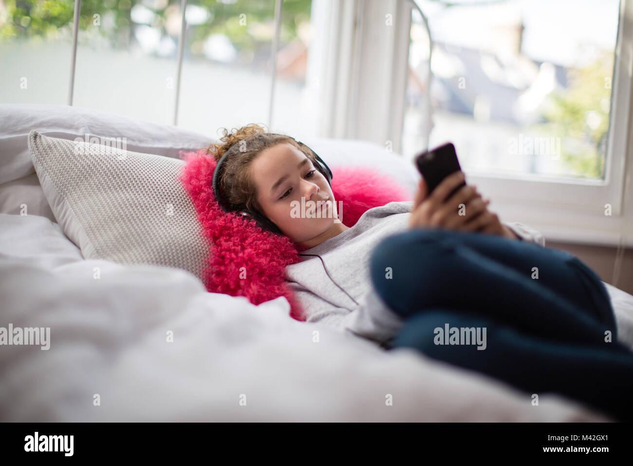 Teenager in bedroom listening to music on smartphone Stock Photo