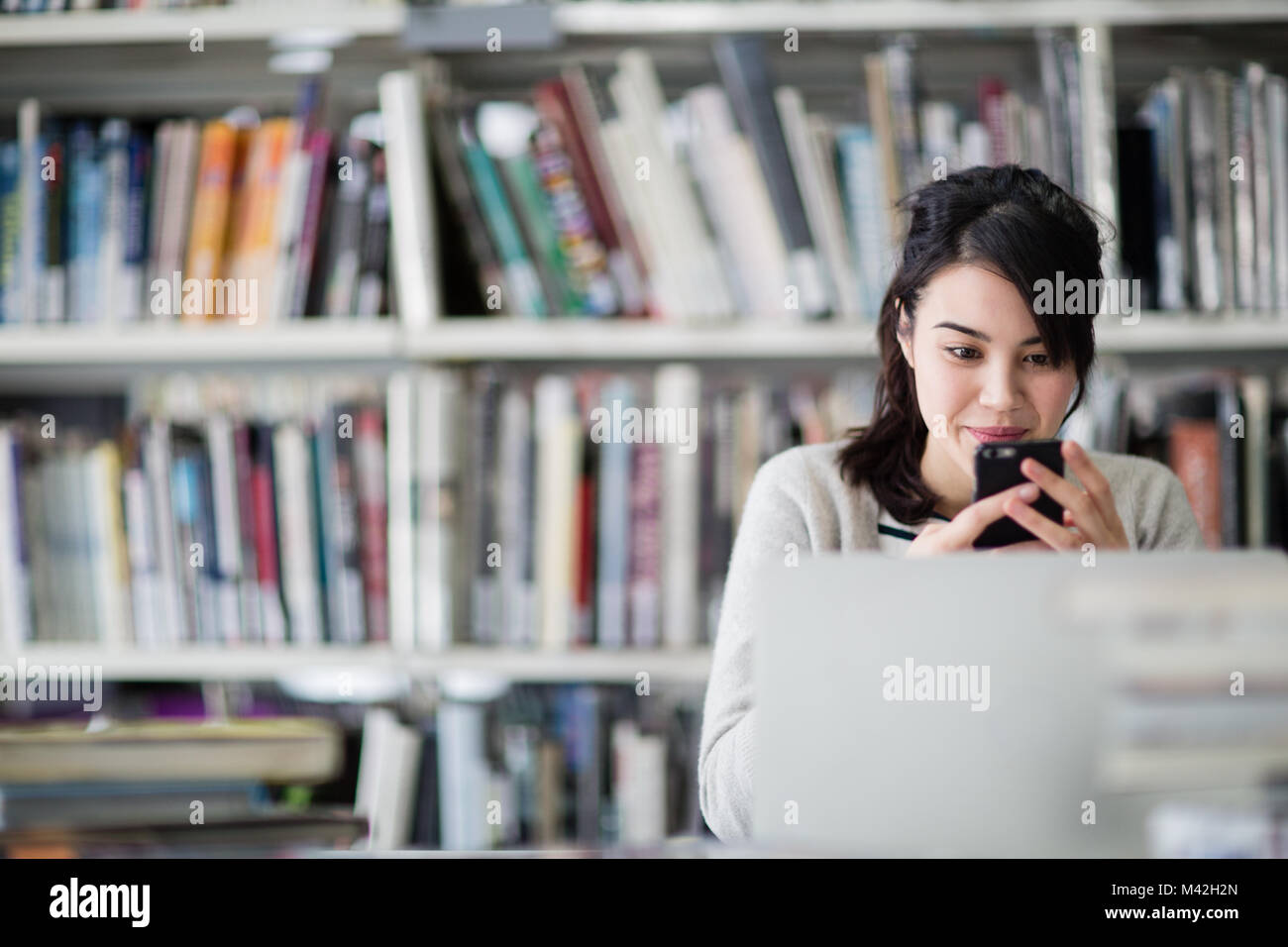 Student using smartphone and laptop in library Stock Photo