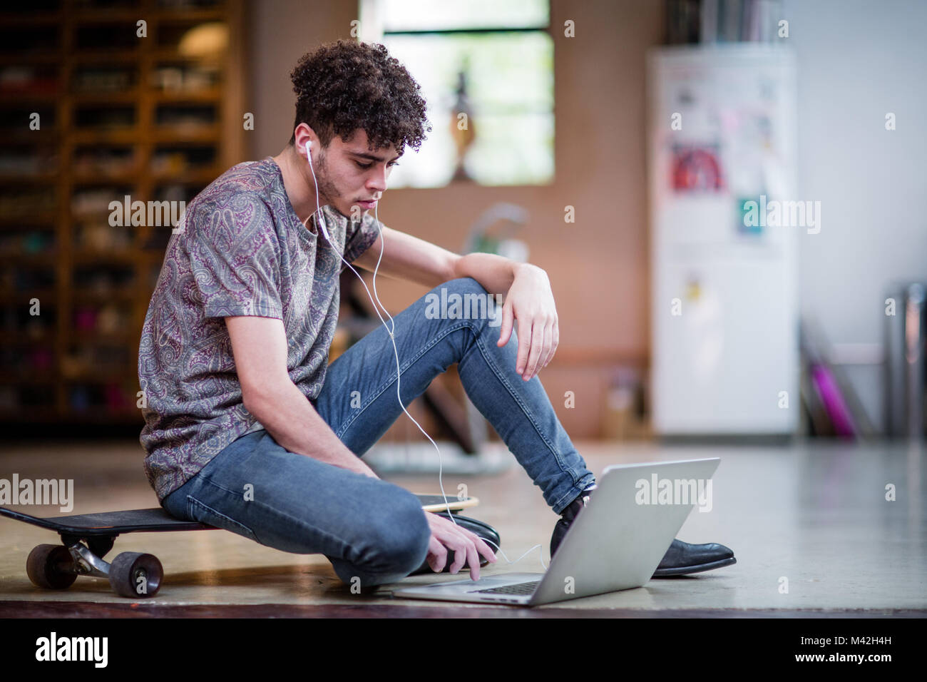 Young adult male sitting on skateboard using laptop Stock Photo