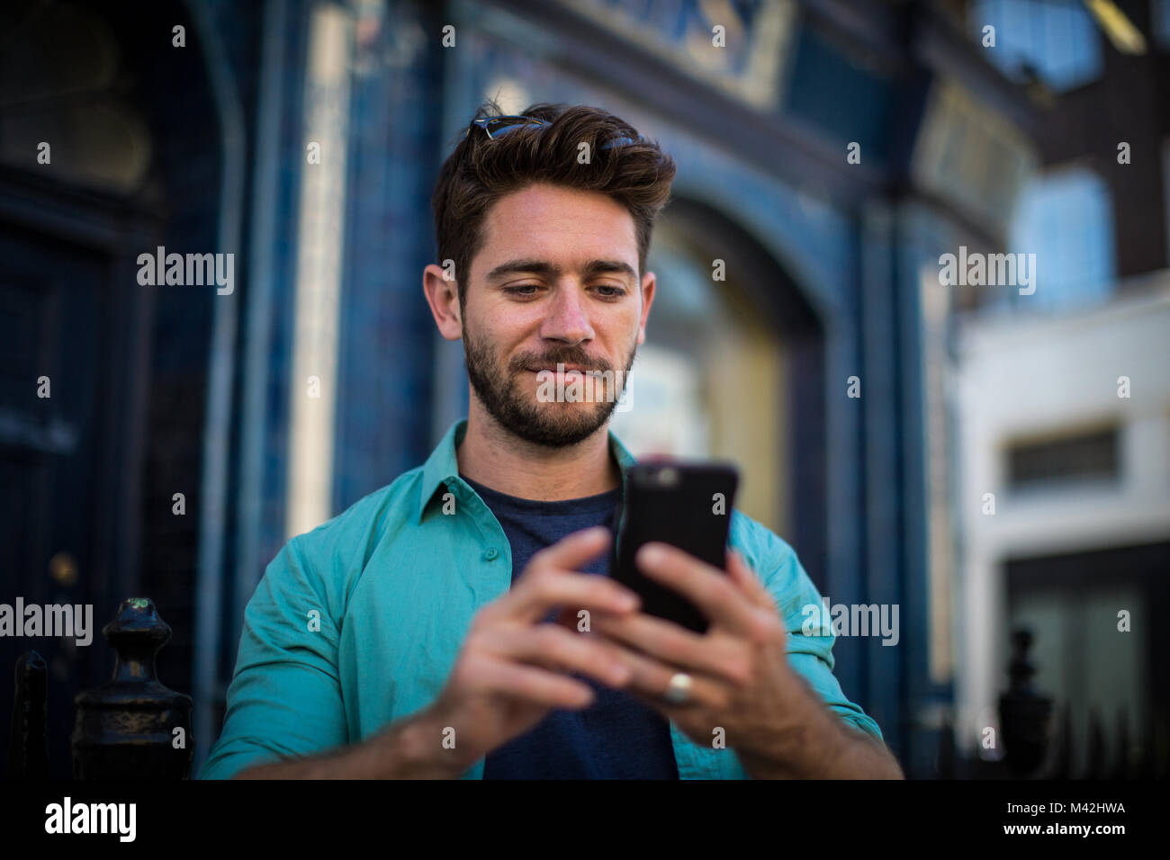 Young adult standing outside London pub using smartphone Stock Photo