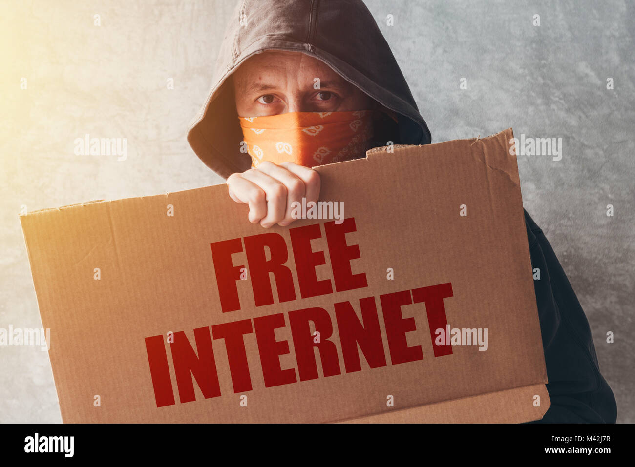 Hooded activist protestor holding Free Internet protest sign. Man with hoodie and scarf over face taking part in activism and fighting for the cause. Stock Photo