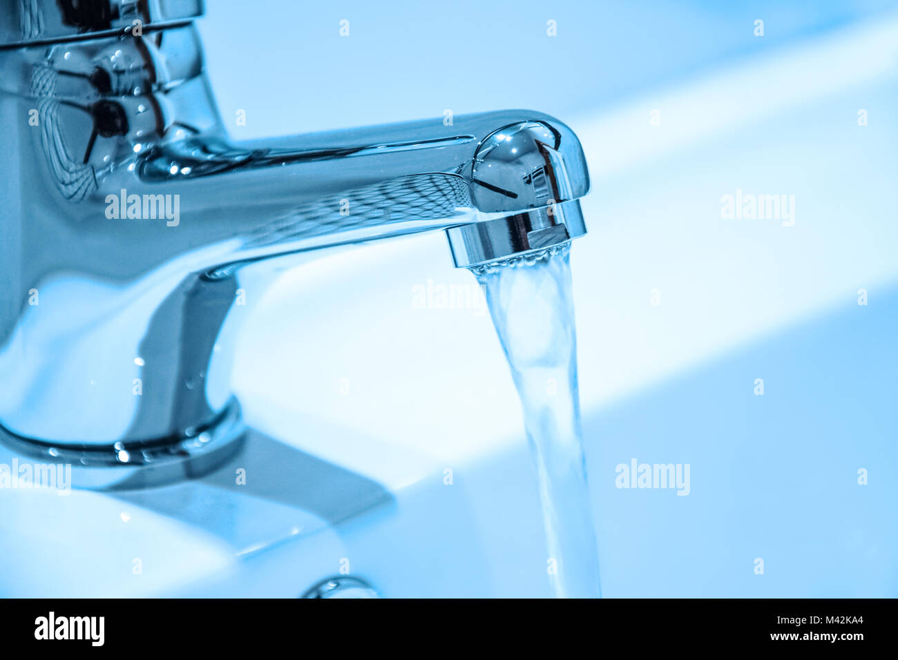 Water running from an open faucet in close-up (blue filter effect). Stock Photo