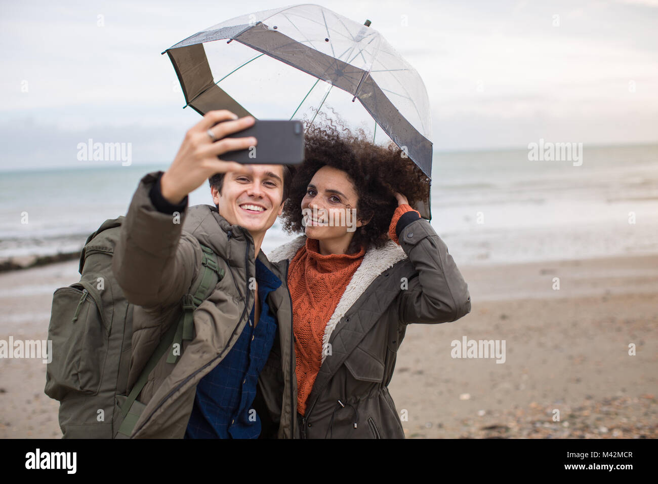 Young couple taking a selfie on a beach in bad weather Stock Photo