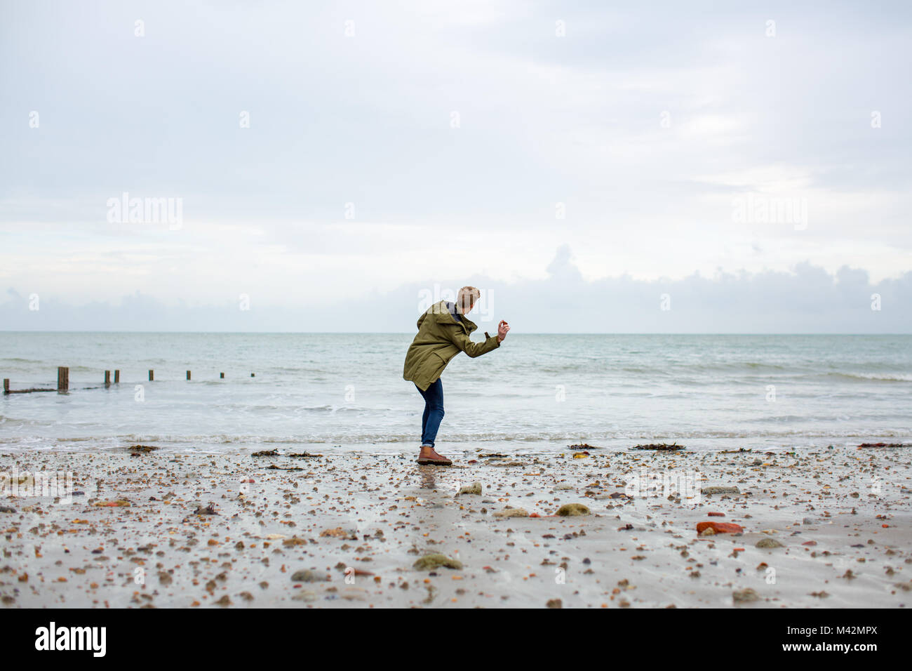 Young male skimming stones on a beach in winter Stock Photo
