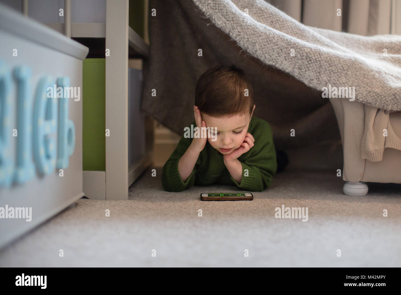 Preschool boy playing with smartphone in den Stock Photo