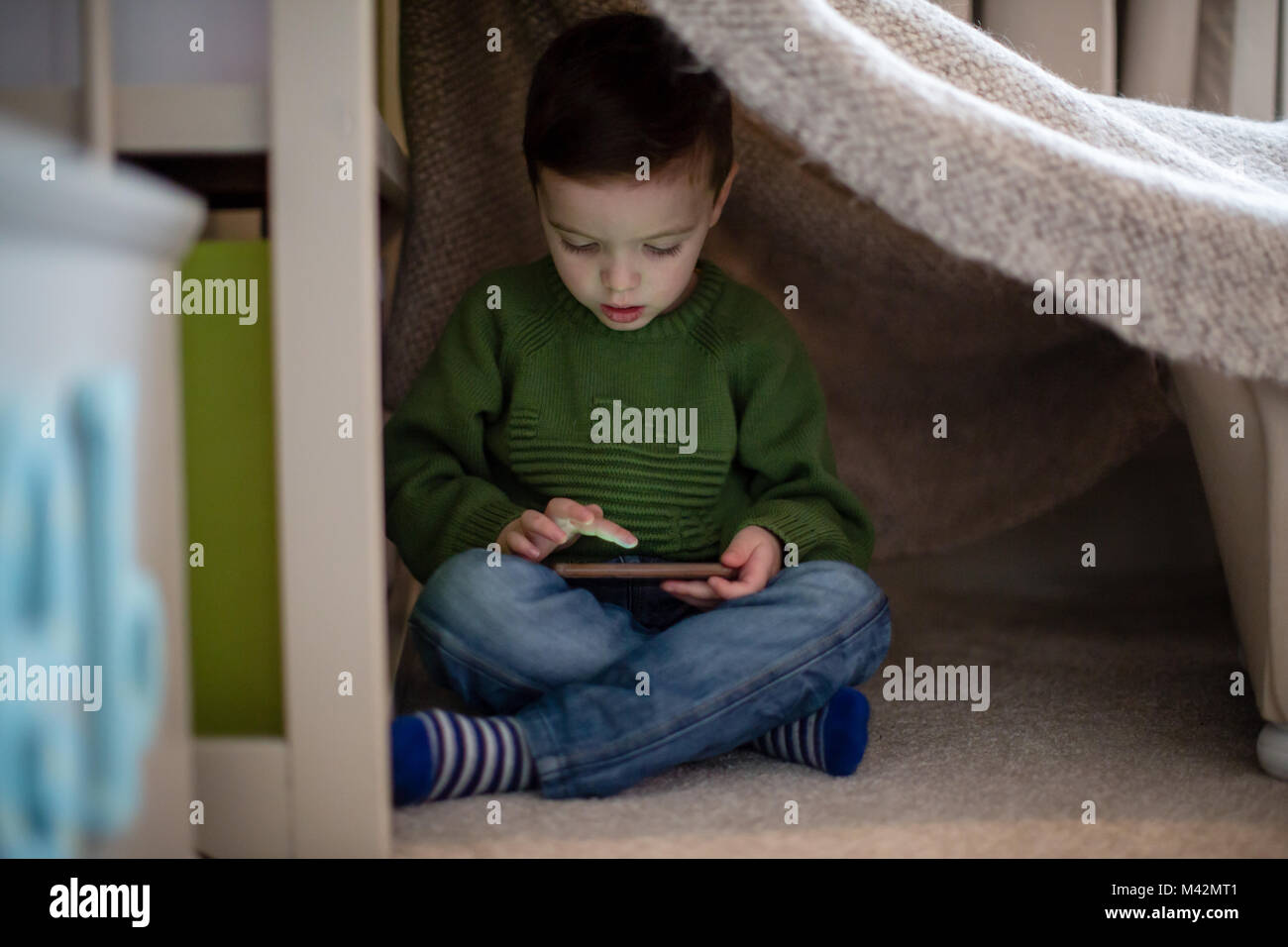 Preschool boy playing with smartphone in den Stock Photo