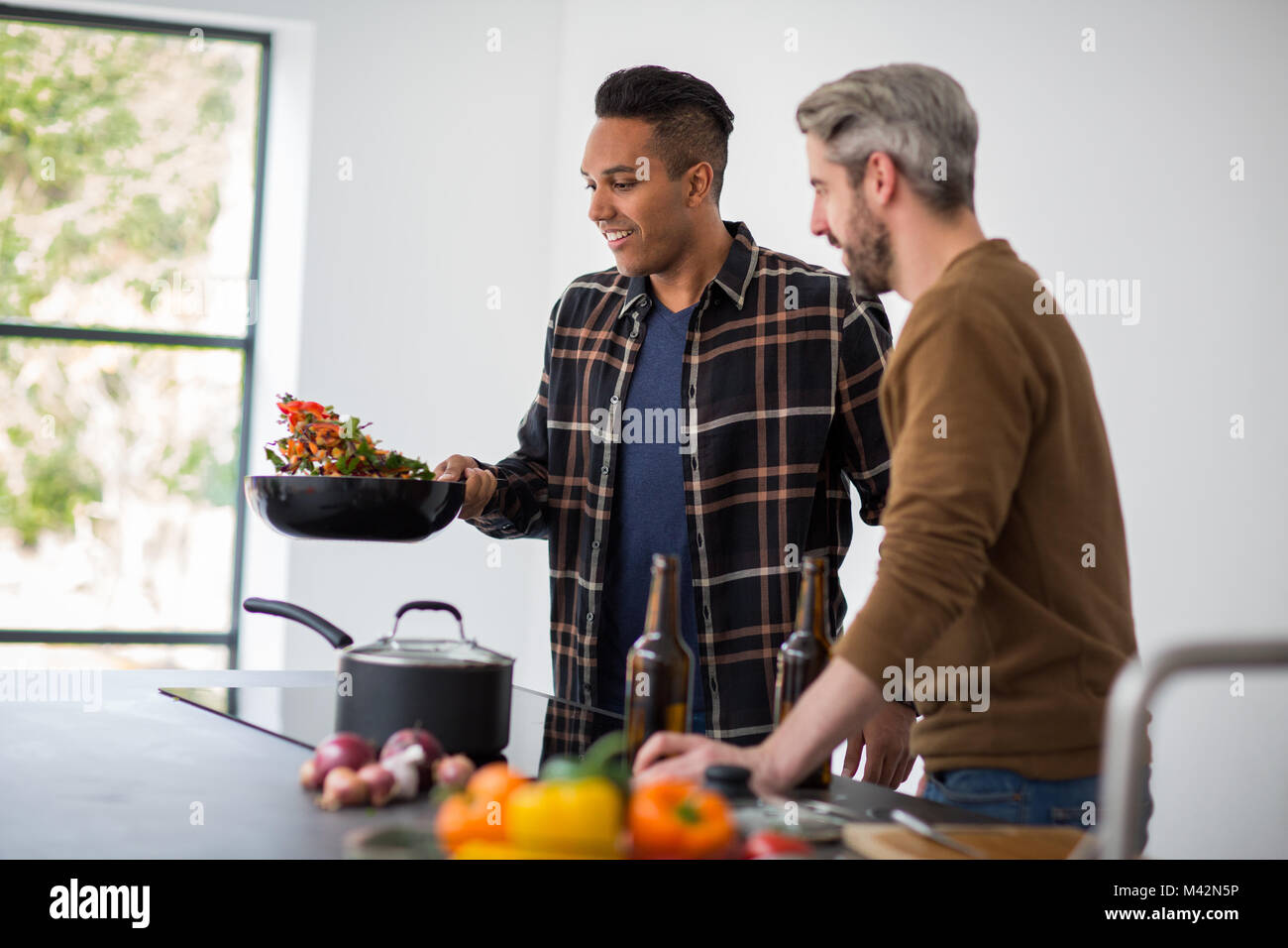 Male friends having a beer whilst cooking a stir fry Stock Photo