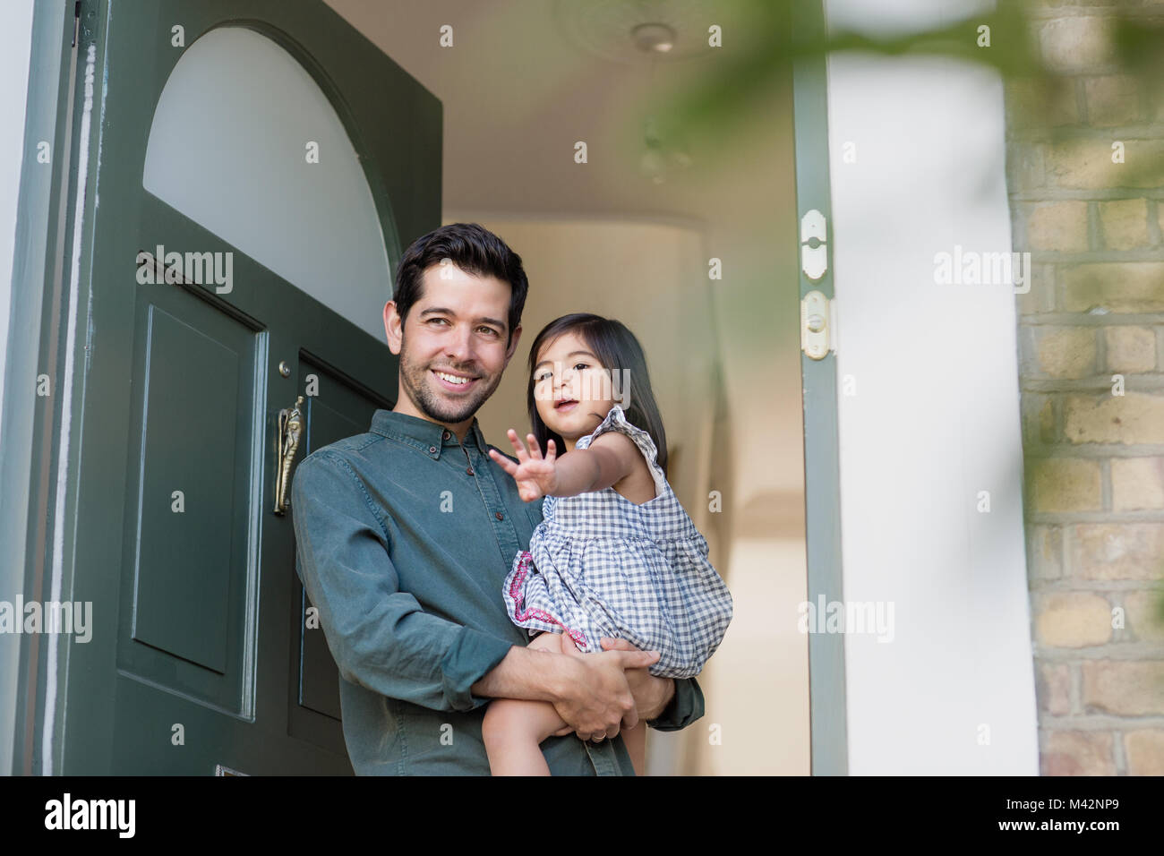 Father standing in home doorway with daughter waving Stock Photo