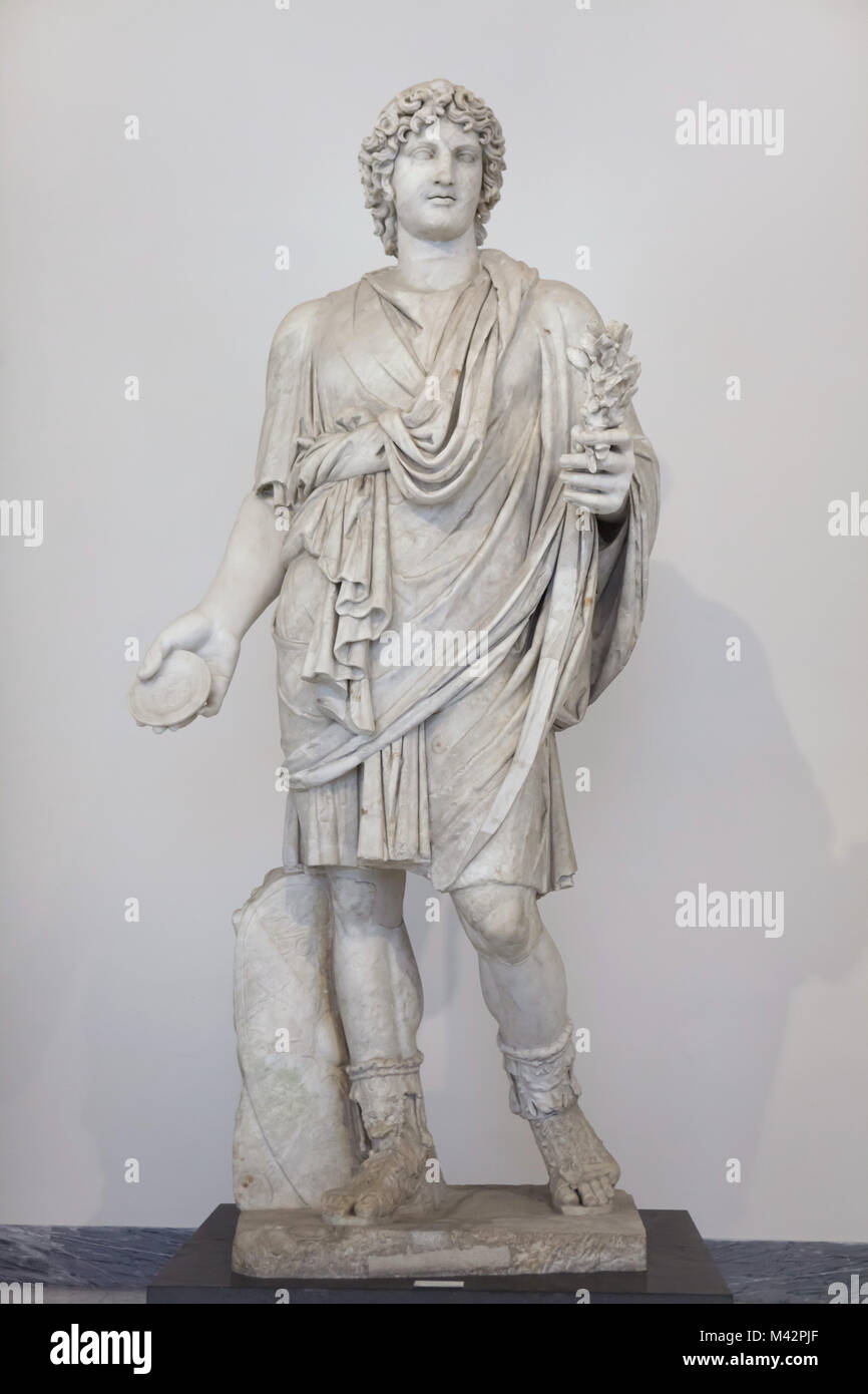 Farnese Lar. Roman marble statue from the 2nd century AD from the Farnese Collection on display in the National Archaeological Museum in Naples, Campania, Italy. Idealized youth addressed in a short tunic with a cloak and holding a patera in his right hand. The statue was restored by Italian sculptor Carlo Albacini. Stock Photo