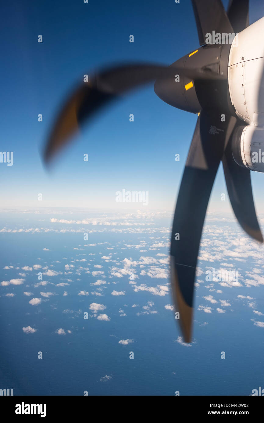 On the way - looking at aeroplane propeller from the aircraft window seat with blue sea and white clouds below Stock Photo