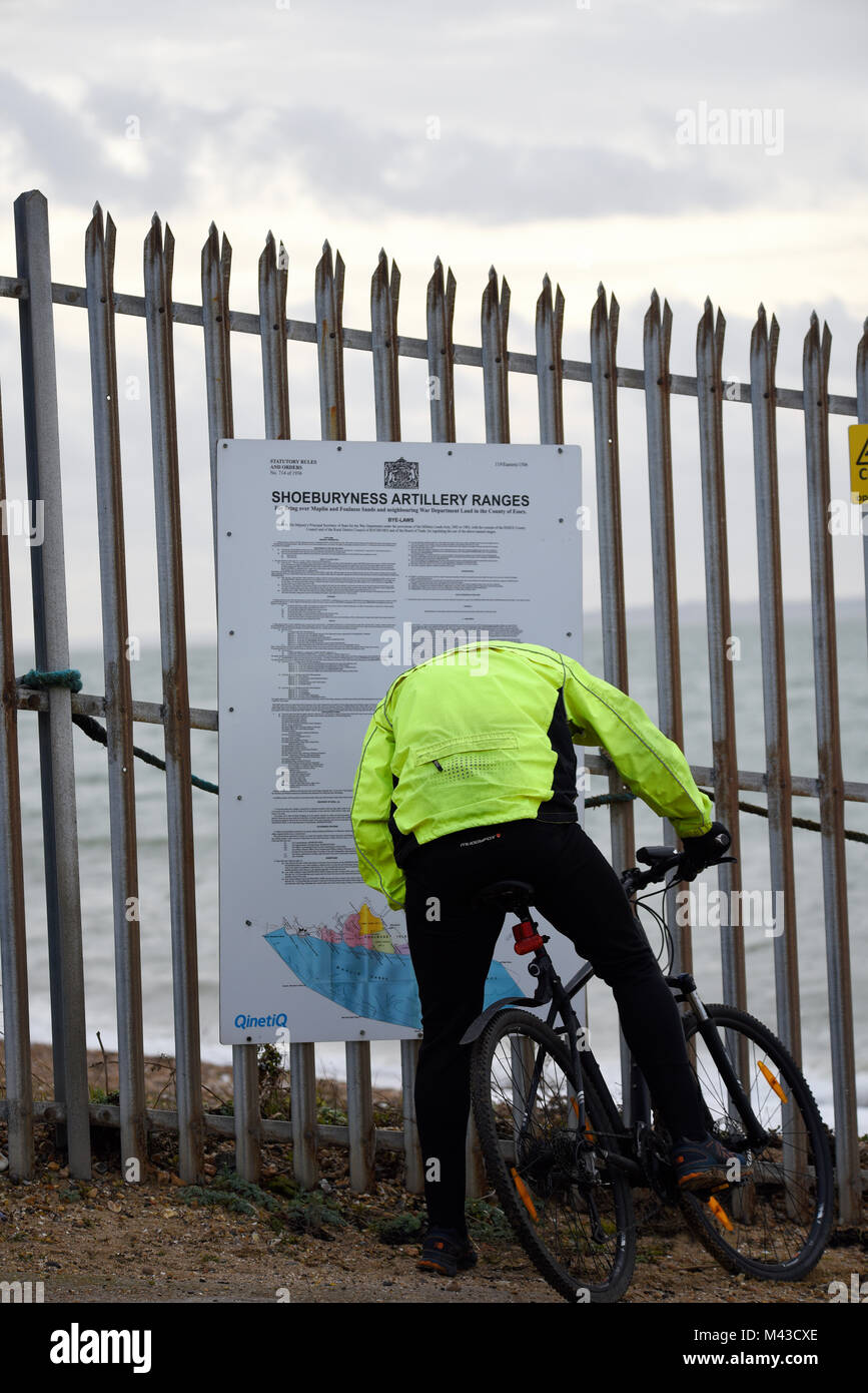 Ministry of Defence firing range at Shoeburyness, with the warning signs ensuring no public access. Cyclist reading danger sign Stock Photo