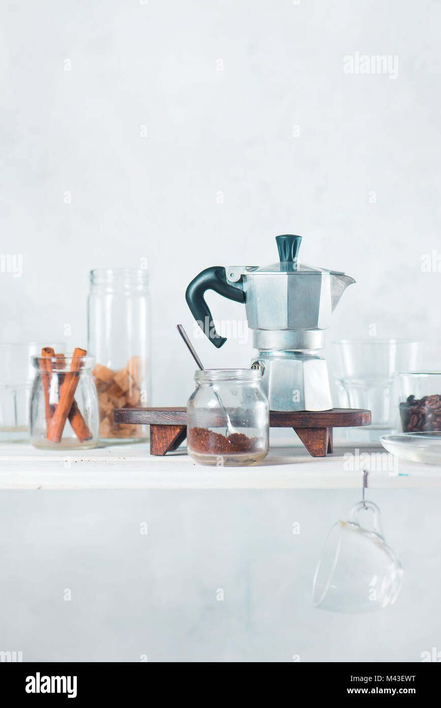 Brewing coffee in Moka pot. White kitchen shelf with dishware and
