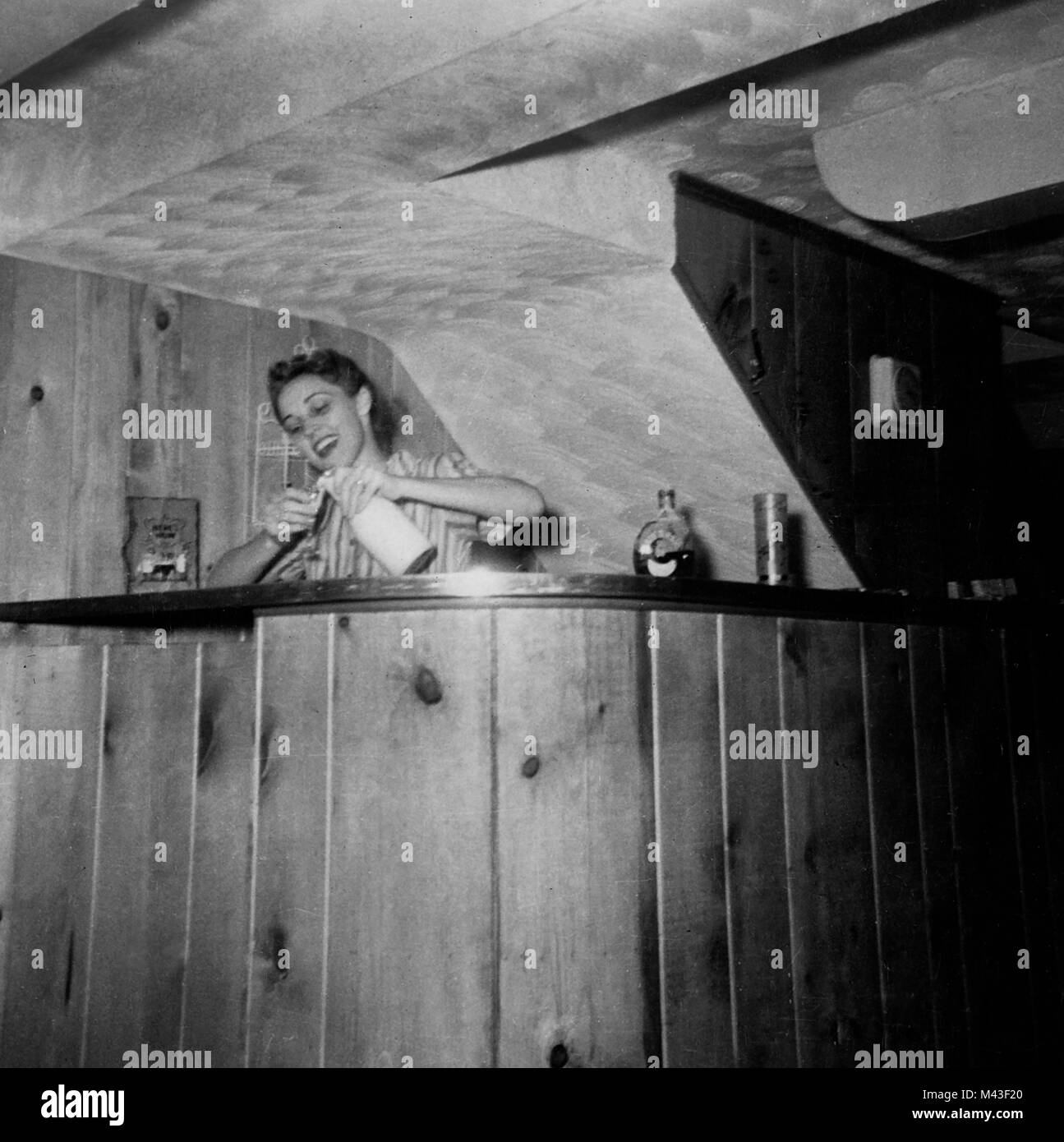 A woman pours a drink in a basement bar, ca. 1955. Stock Photo