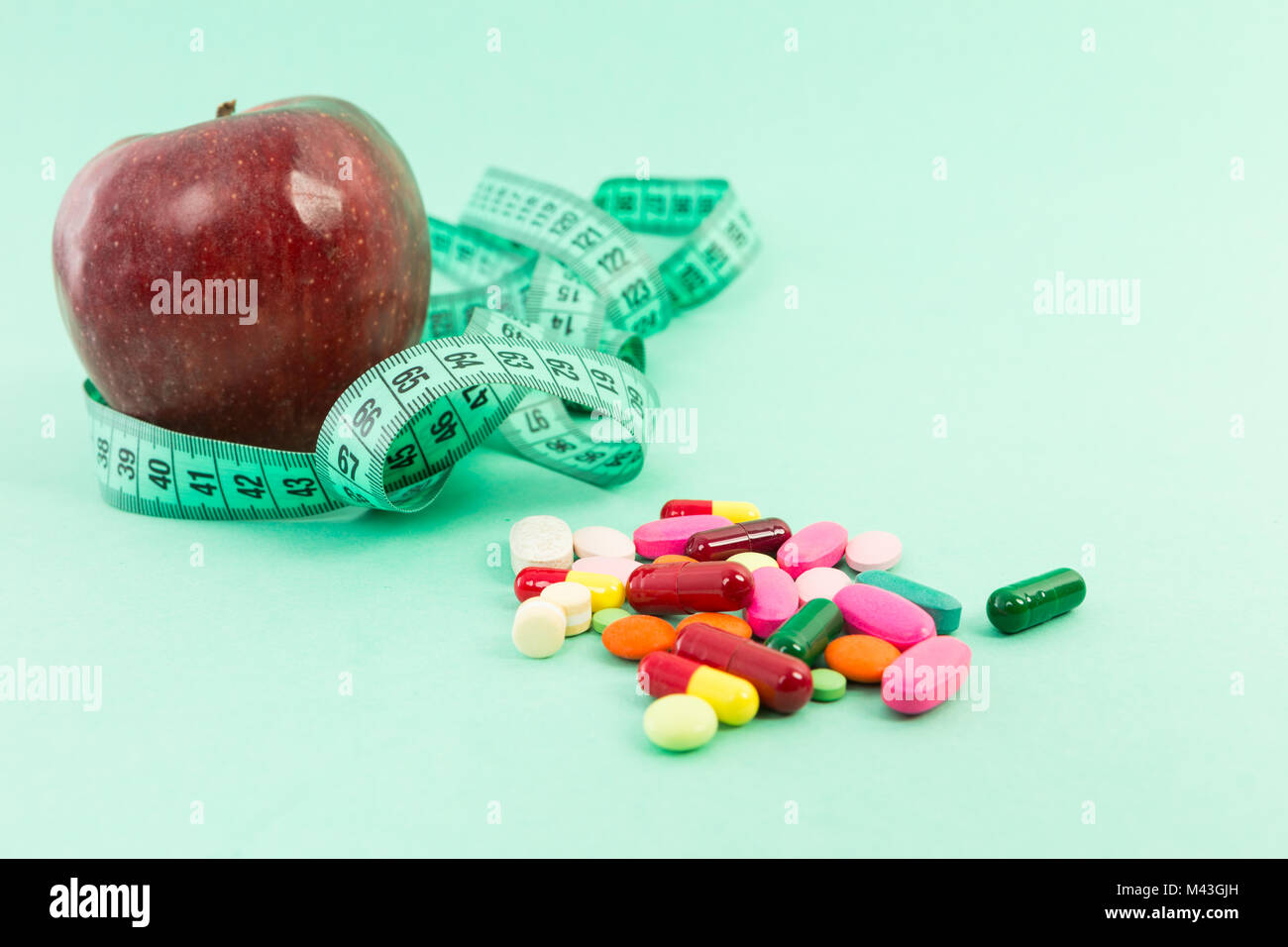 Dieting concept with natural apple, measuring tape and pills or tablets on medical green background Stock Photo