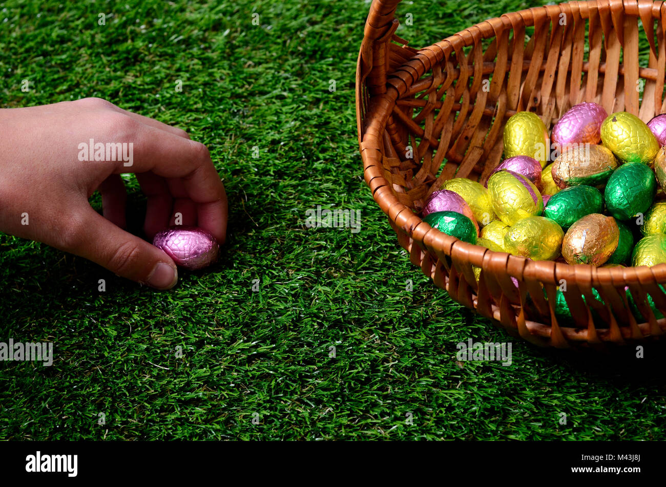 Hand picking easter egg on grass, and chocolate easter eggs basket