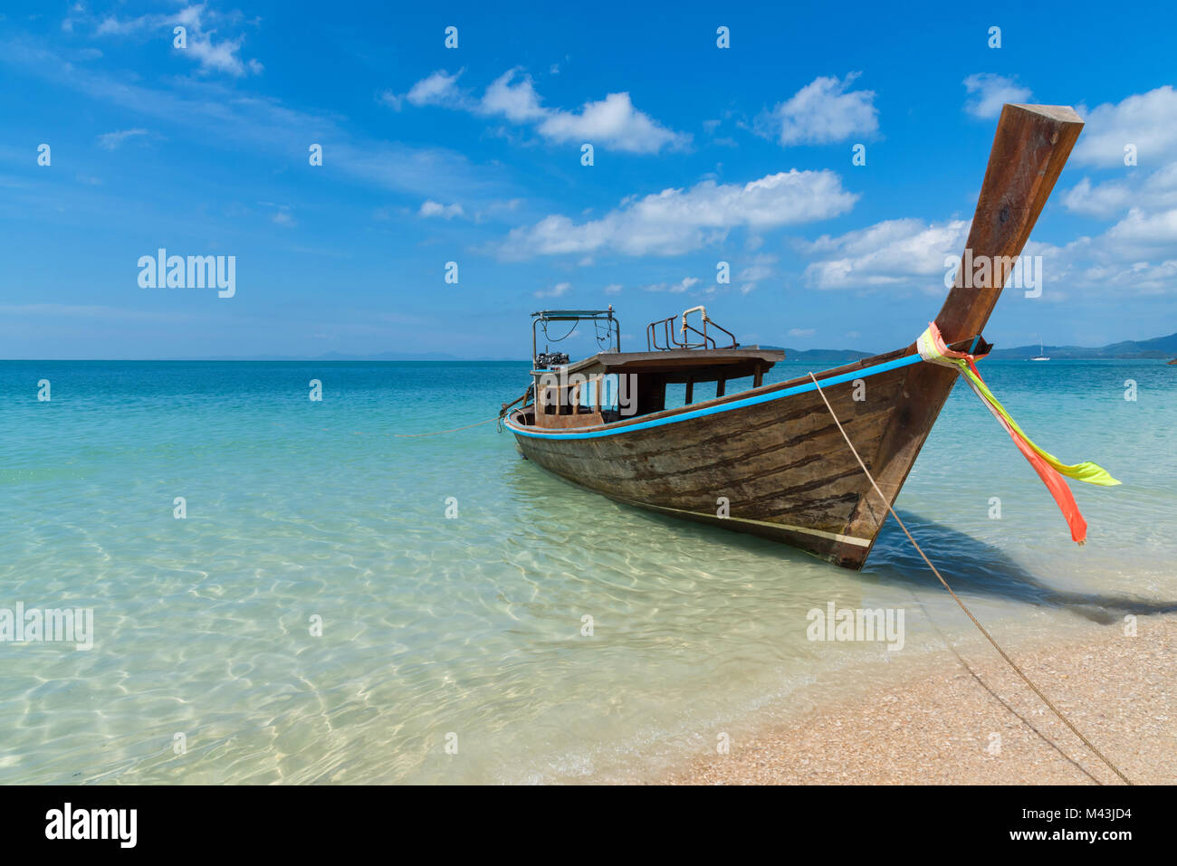 Stunning landscape shot of a paradise destination- lone longtail boat at the shore of a sandy beach in Thailand with clear blue ocean water Stock Photo