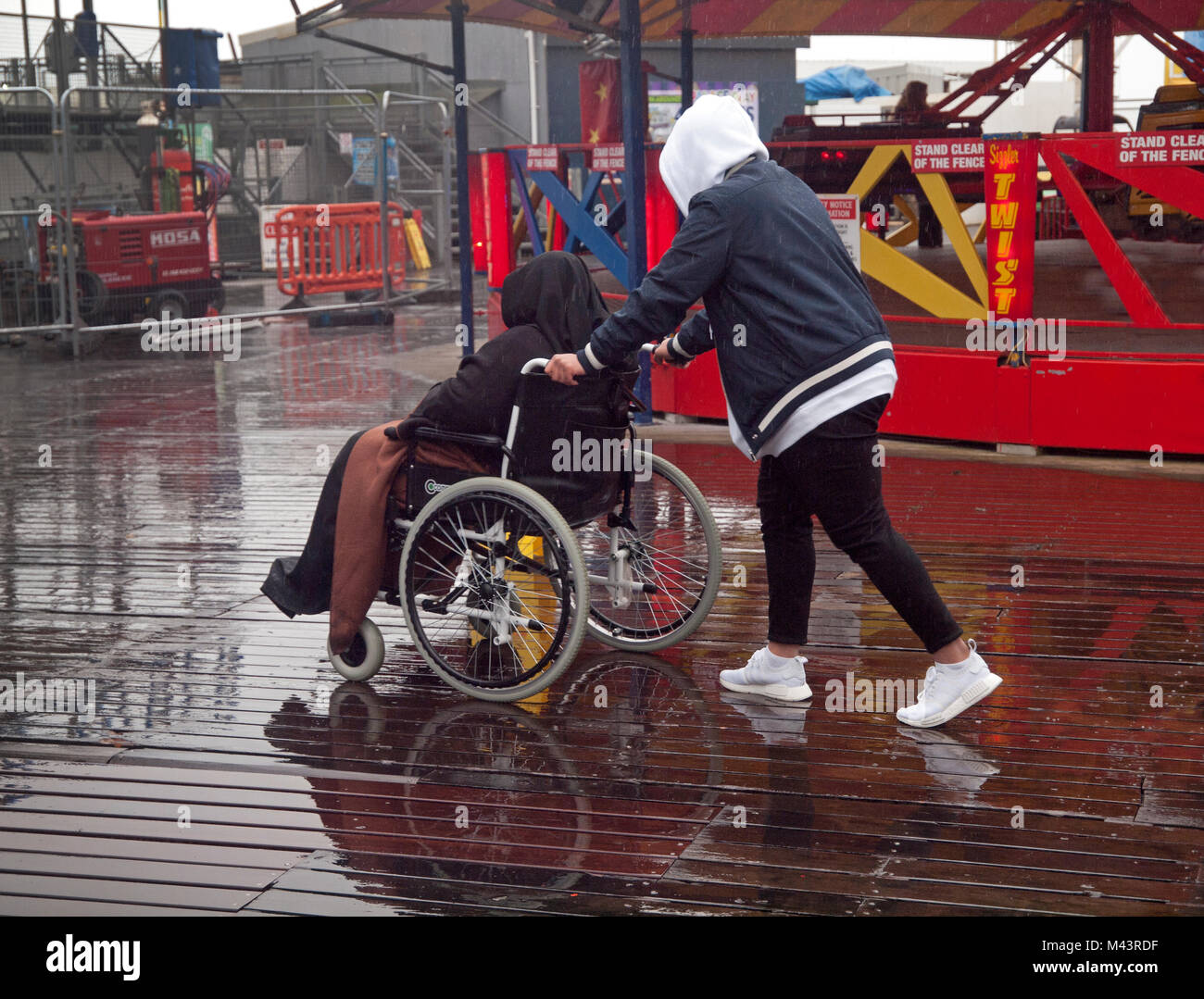 On a wet day a wheelchair is pushed around the pier in Brighton Stock