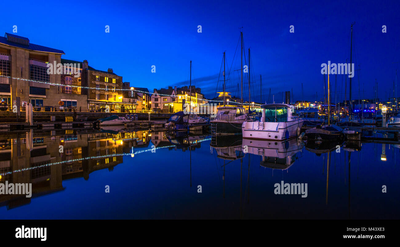 A view of various fishing boats and pleasure craft reflected in mirror like water at Sutton Harbour on Plymouth's historic Barbican. Stock Photo