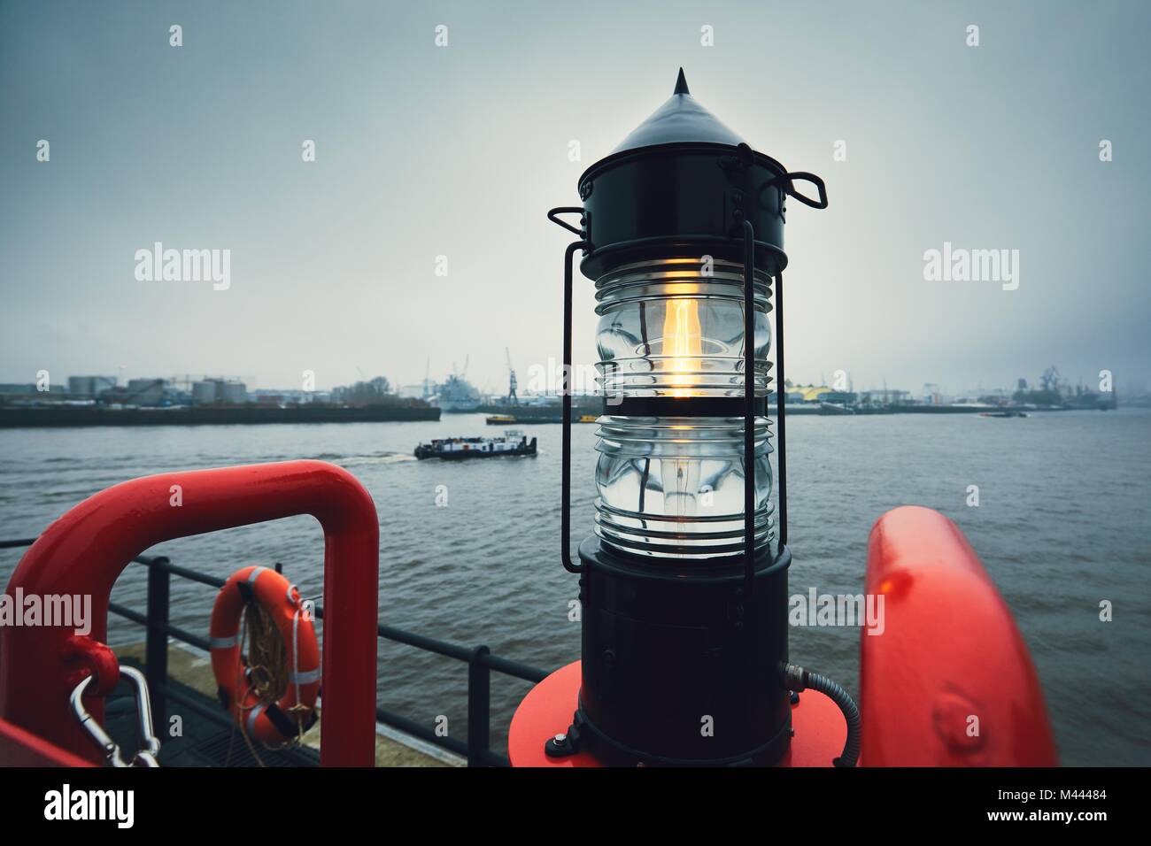 Beacon against freight ship and harbor. Gloomy and cold day in Hamburg, Germany Stock Photo