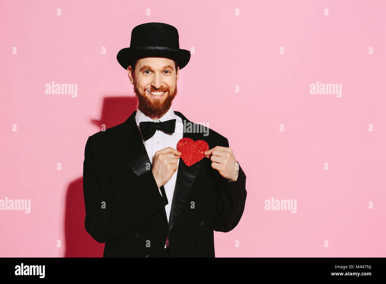 Smiling man in a tuxedo and top hat holding a red heart Stock Photo