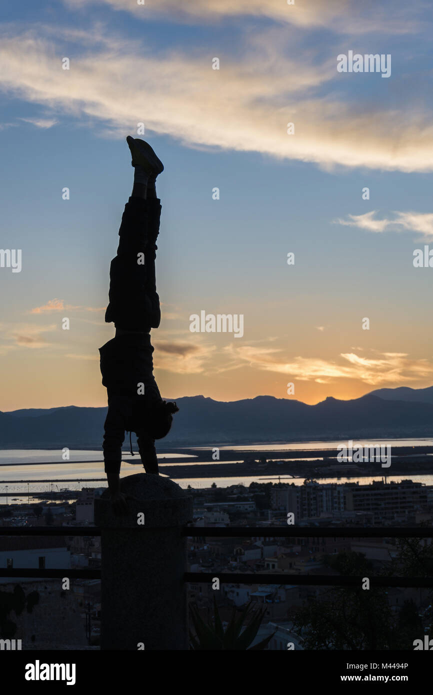 Silhouette of man doing handstand on railing, Cagliari, Sardinia, Italy Stock Photo
