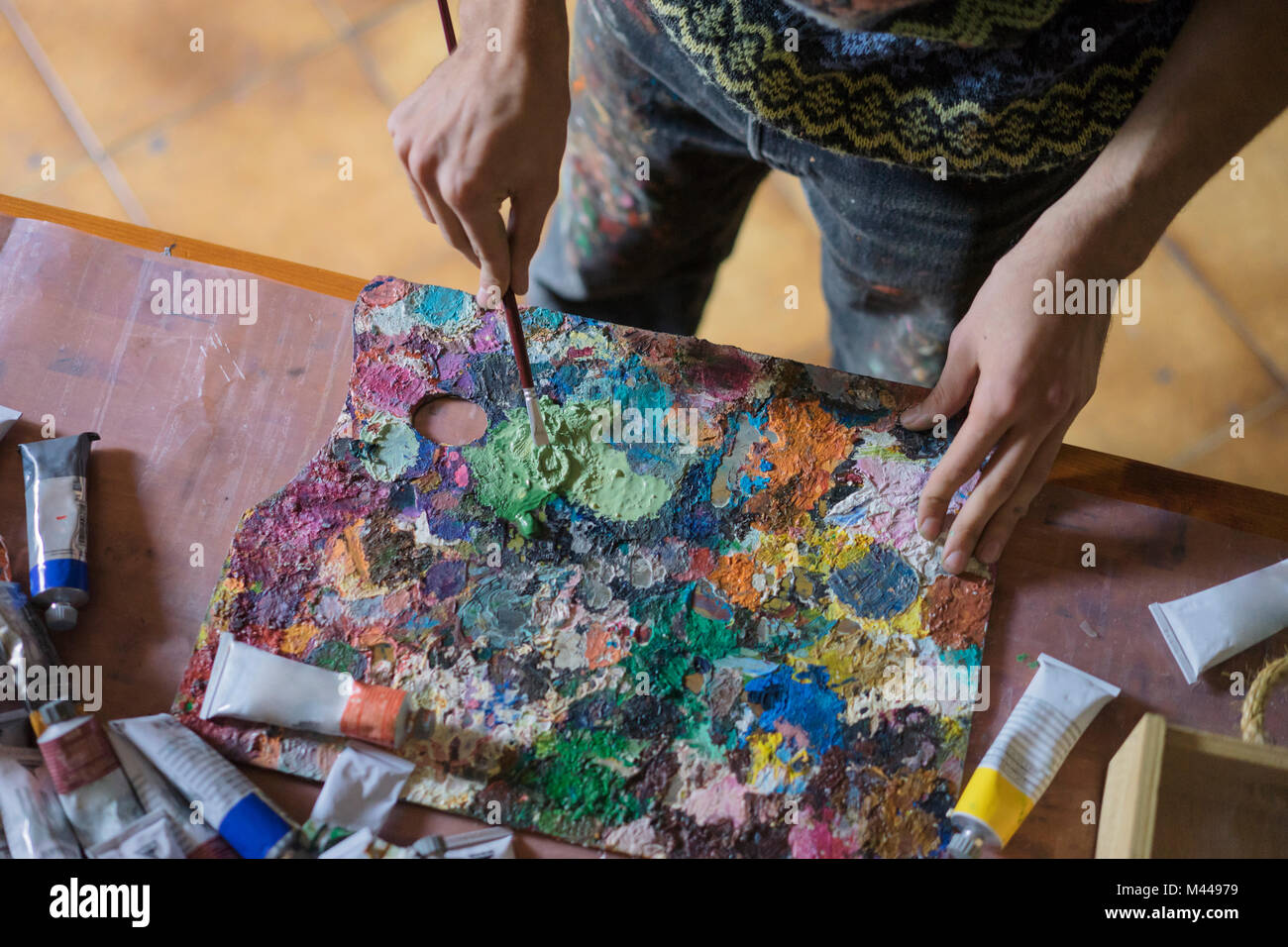 Male artist mixing oil paint on palette in artists studio, mid section