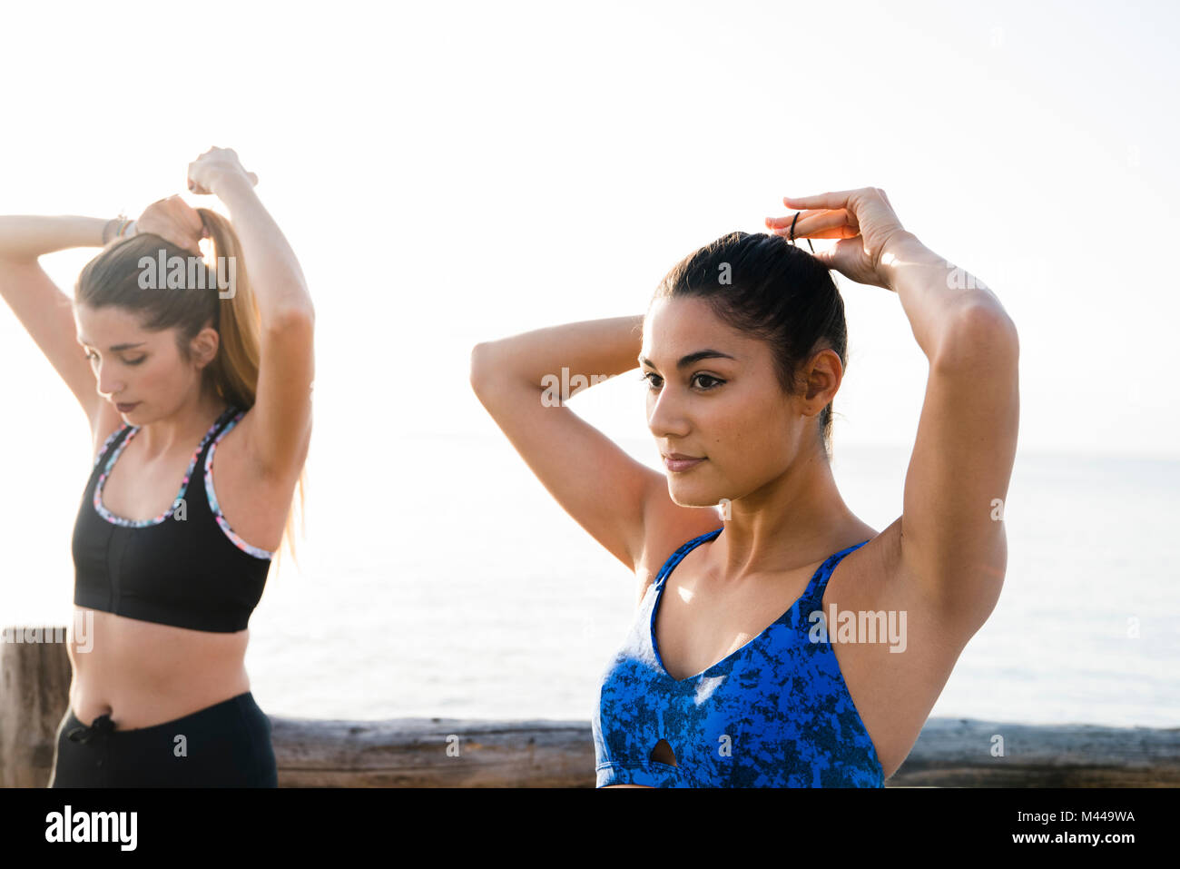 Two young women training on beach, tying hair ponytails Stock Photo