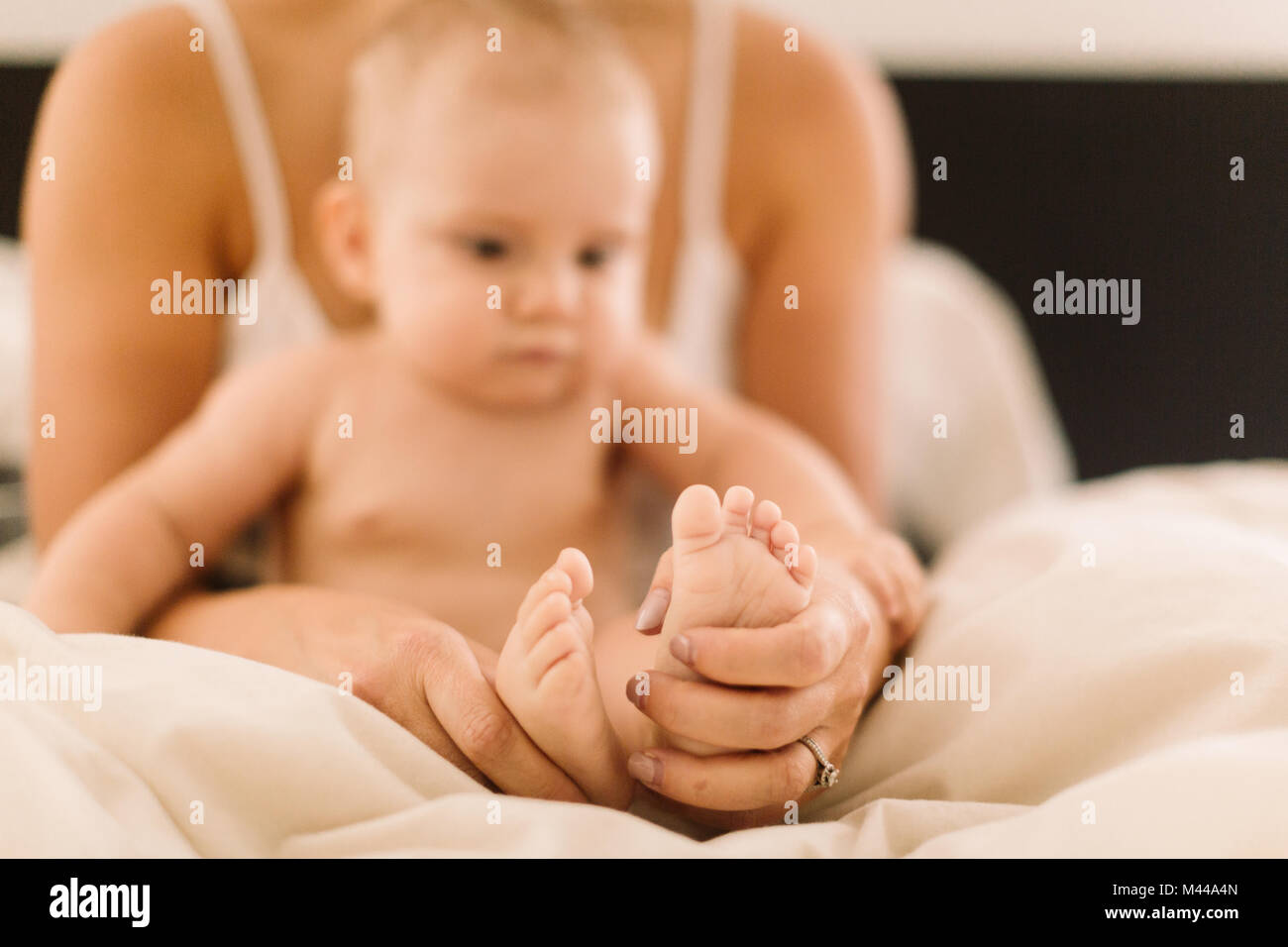 Woman holding baby daughters bare feet on bed, close up Stock Photo