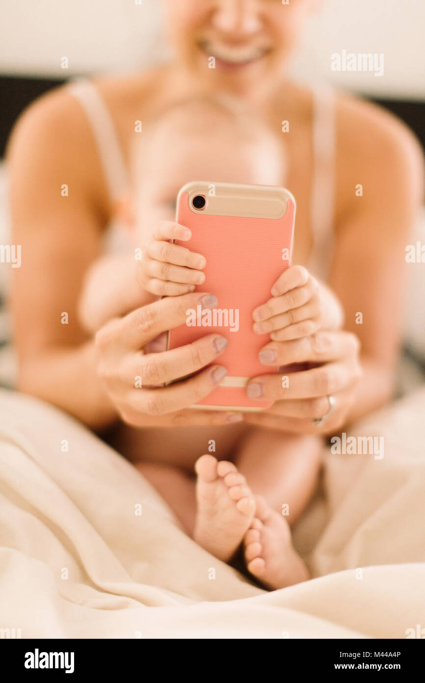Baby girl and mother's hands gripping smartphone, close up Stock Photo