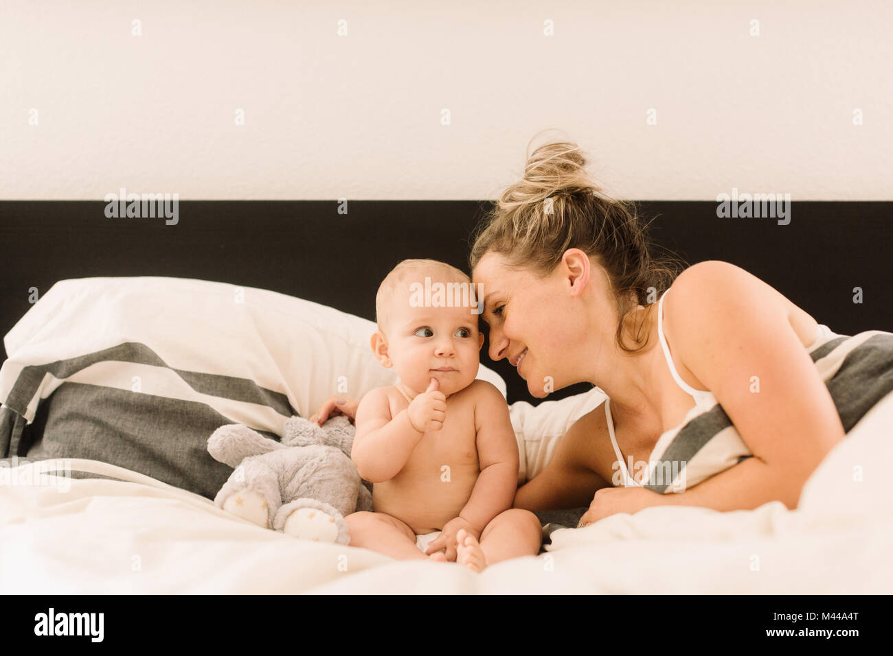 Woman lying in bed with arm around baby daughter Stock Photo