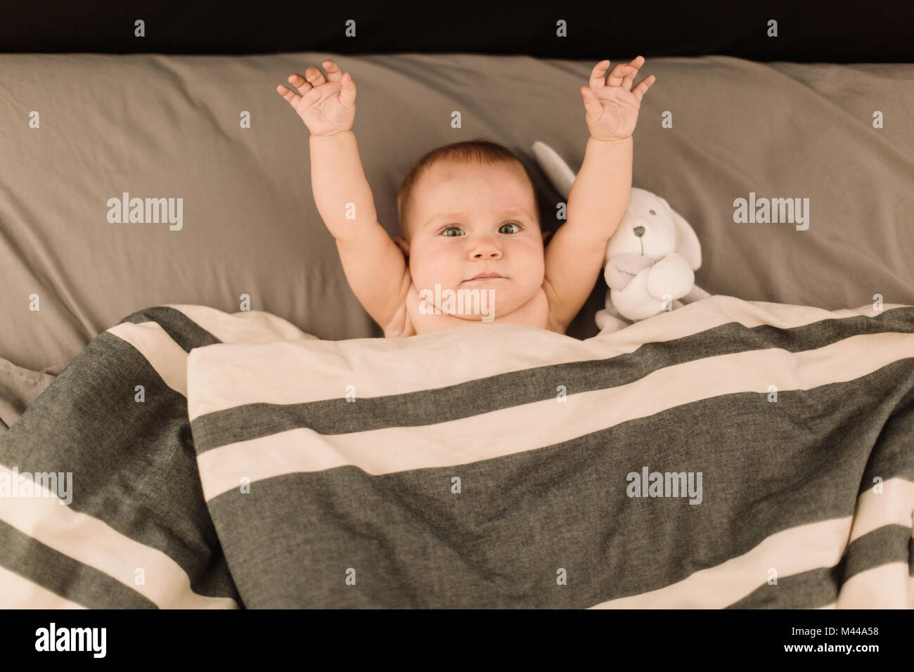 Portrait of baby girl lying in bed with arms raised, overhead view Stock Photo