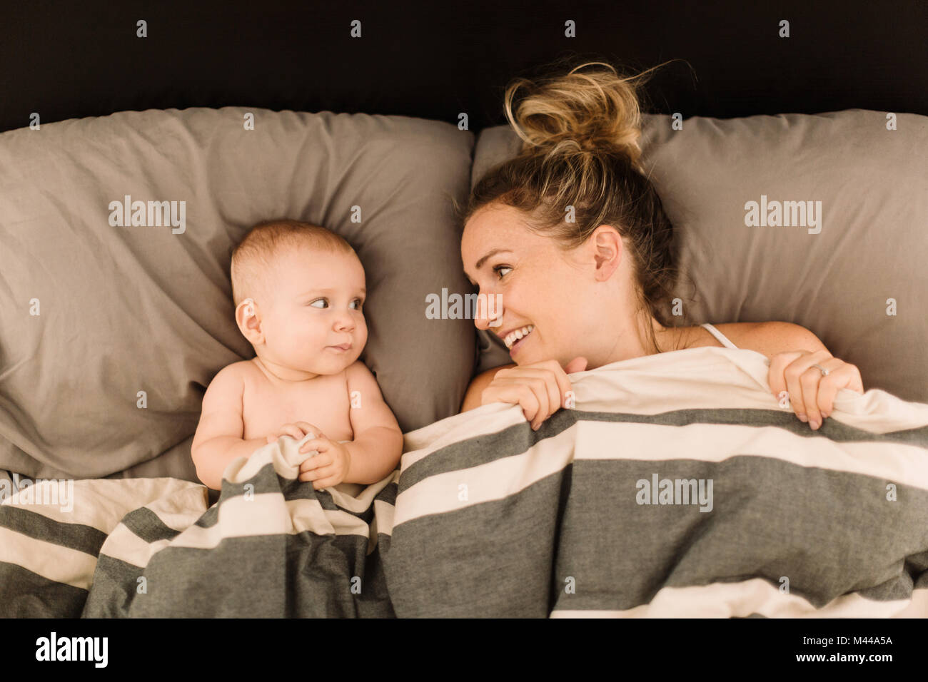 Woman lying in bed under duvet with baby daughter, overhead view Stock Photo
