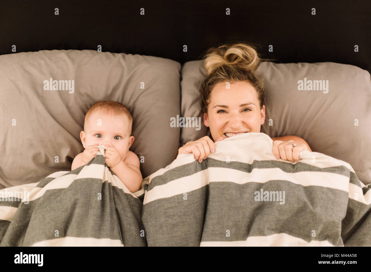 Portrait of woman lying in bed under duvet with baby daughter, overhead view Stock Photo