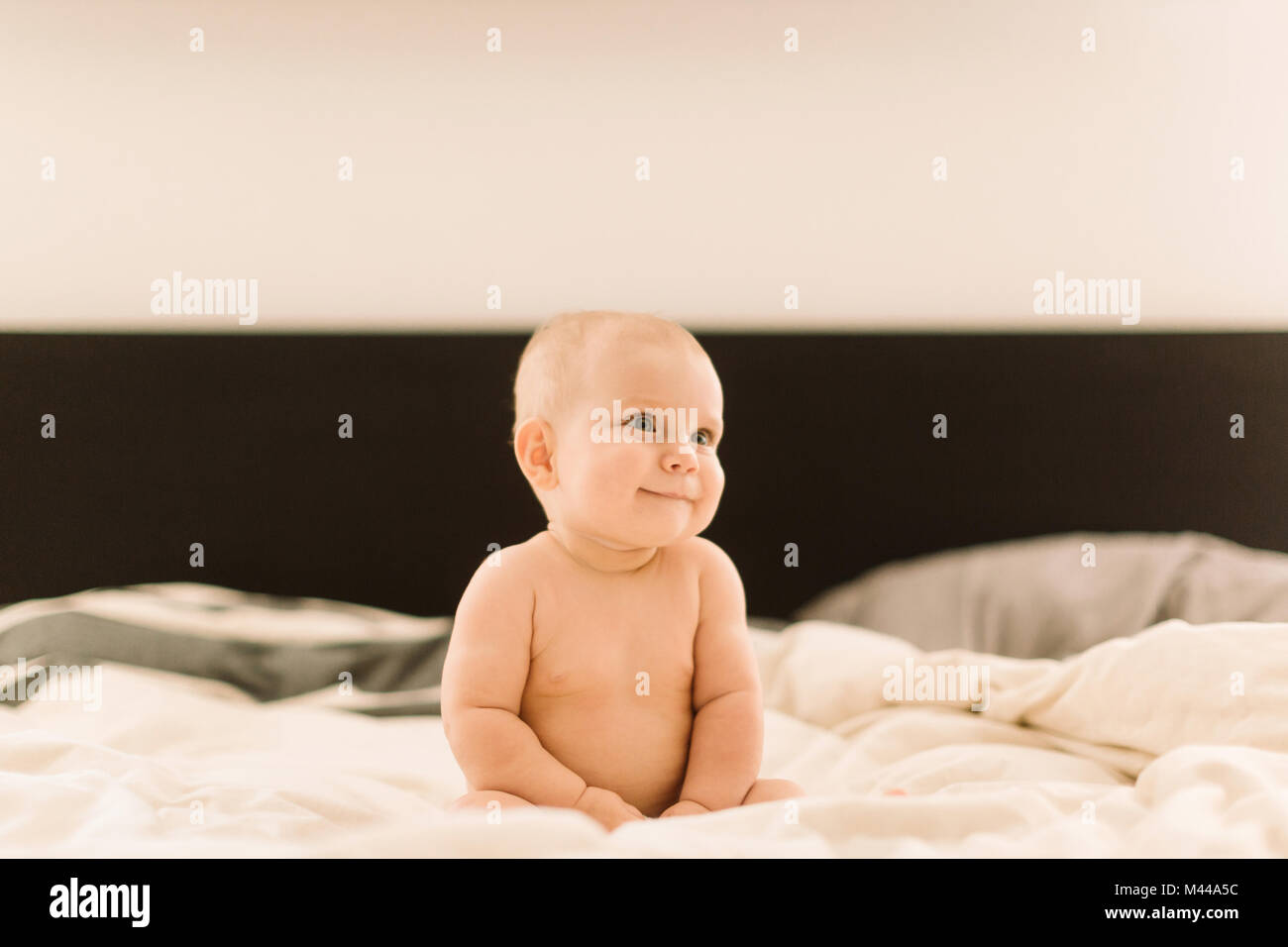 Cute baby girl sitting up on bed looking away Stock Photo