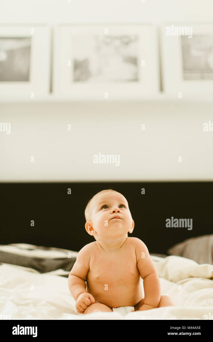 Cute baby girl sitting up on bed looking up Stock Photo