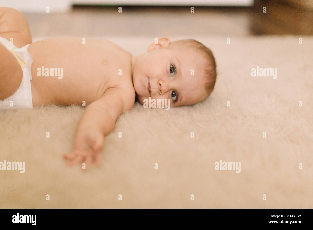 Portrait of cute baby girl in diaper lying on beige rug Stock Photo