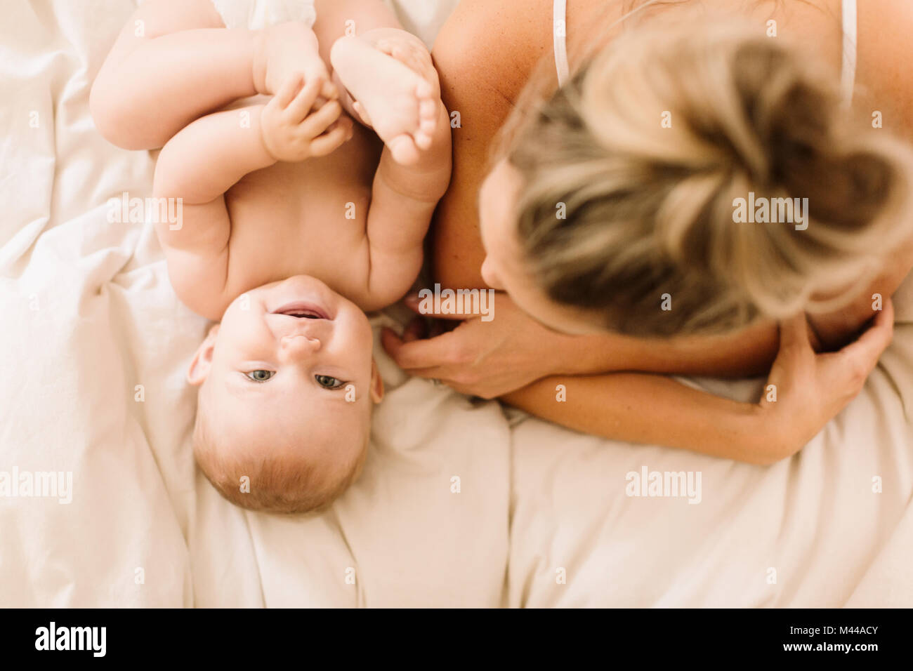 Overhead portrait of cute baby girl lying on bed with mother Stock Photo