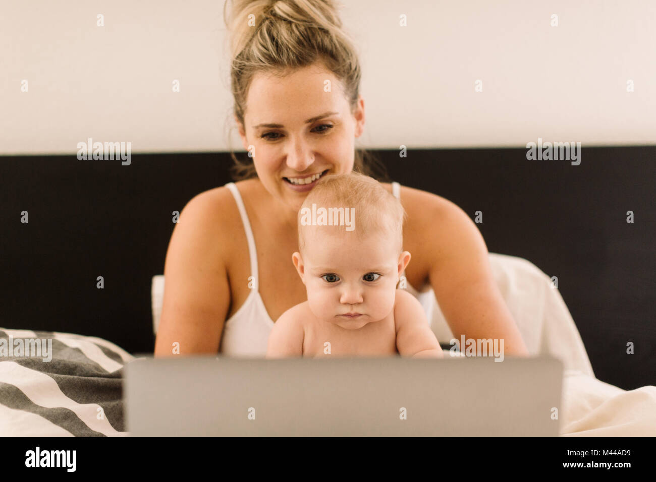 Baby girl and mother sitting up in bed staring at laptop Stock Photo