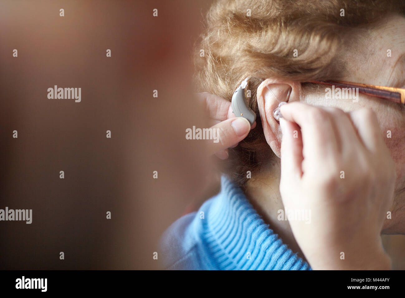 Mature woman helping senior woman insert hearing aid, close-up, differential focus Stock Photo