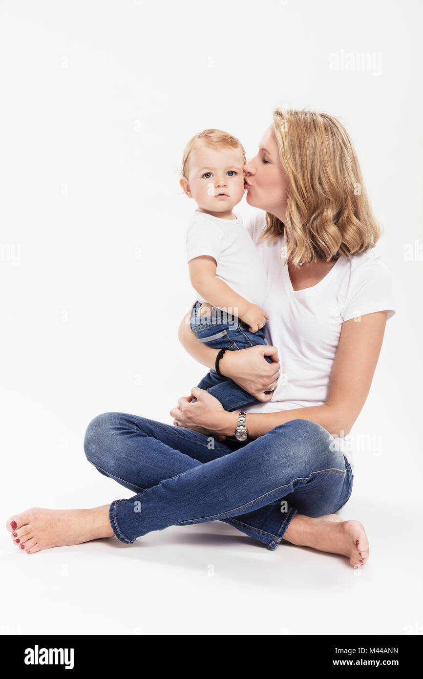 Studio portrait of woman sitting cross legged on floor kissing baby son Stock Photo