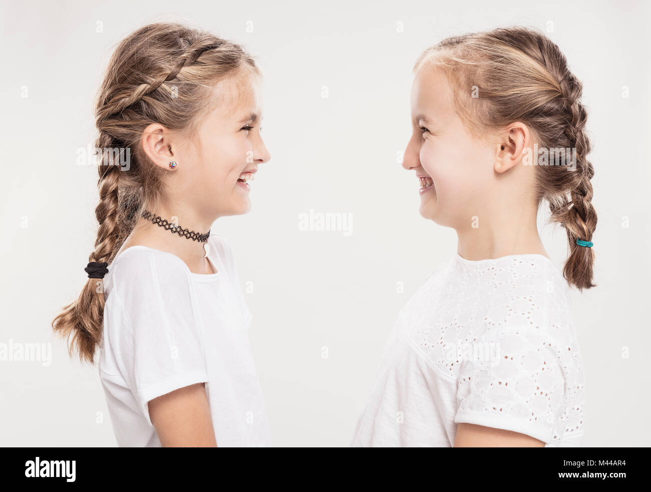 Studio portrait of two girls with hair plaits face to face, head and shoulders Stock Photo