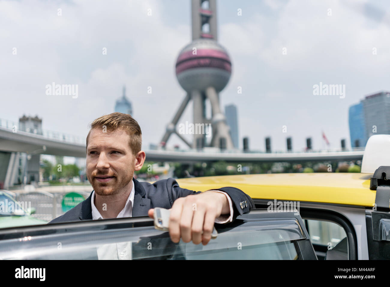 Young businessman getting out of yellow cab at Shanghai financial centre, Shanghai, China Stock Photo