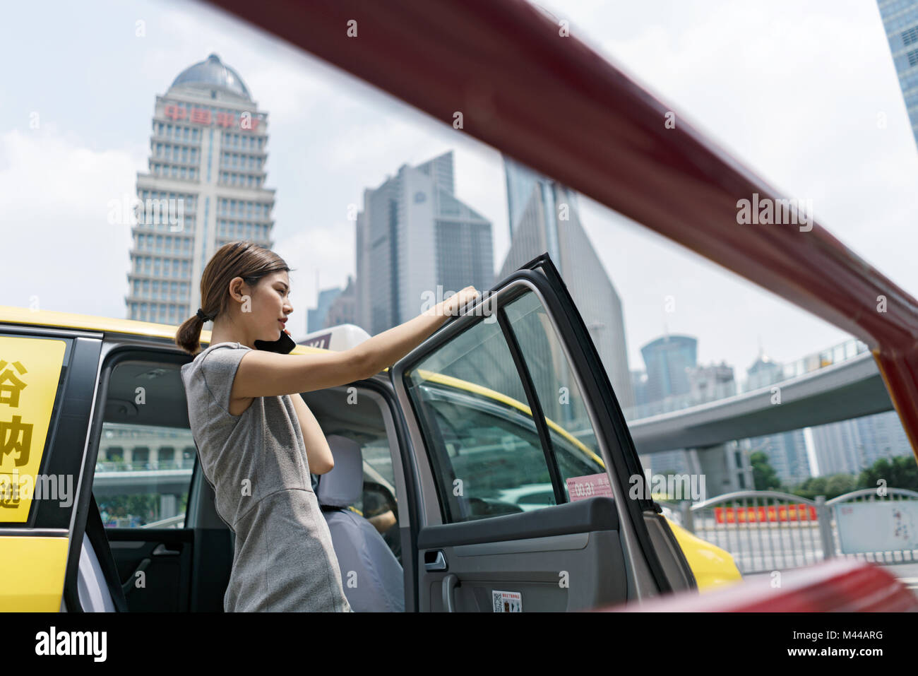 Young businesswoman getting out of yellow cab at Shanghai financial centre, Shanghai, China Stock Photo