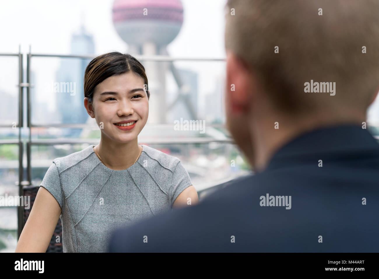 Over shoulder view of young businesswoman and man having meeting at sidewalk cafe in Shanghai financial centre, Shanghai, China Stock Photo
