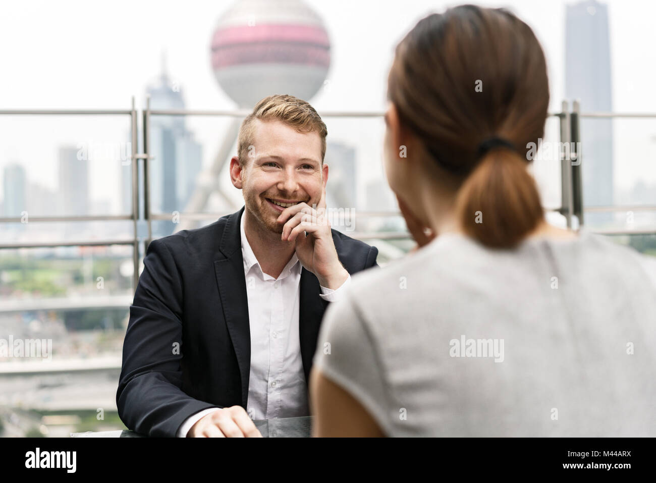 Over shoulder view of young businessman and woman having meeting at sidewalk cafe in Shanghai financial centre, Shanghai, China Stock Photo