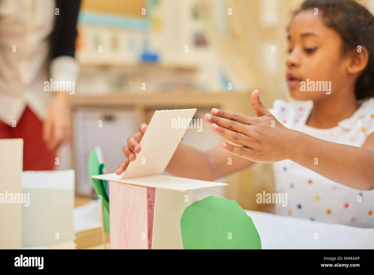 Primary schoolgirl making cardboard structure on classroom desk Stock